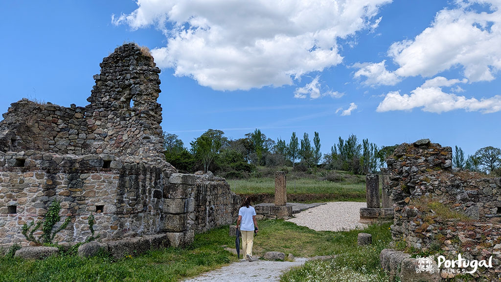 Uma pessoa caminha entre antigas ruínas de pedra sob um céu parcialmente nublado em Marvão, o que visitar os rodeia - verde e charme histórico e pacífico.