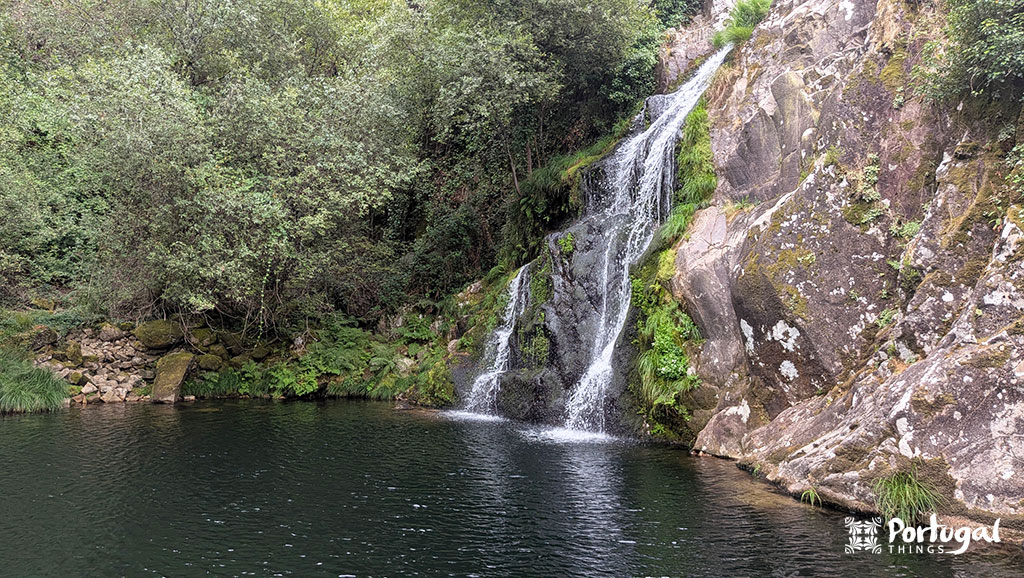 Where to Swim in Gerês National Park: 20 Best Natural Pools 19 A waterfall and a pool with dark green water, surrounded by rocks and lush vegetation.