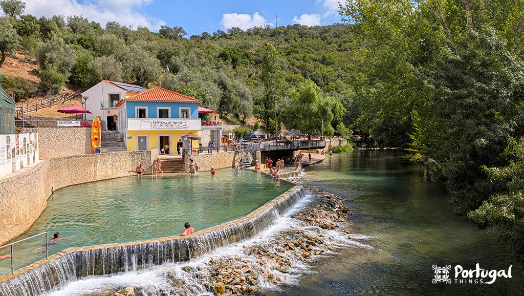 A pool surrounded by the river, with a swimming area. In the background, we have a blue house.