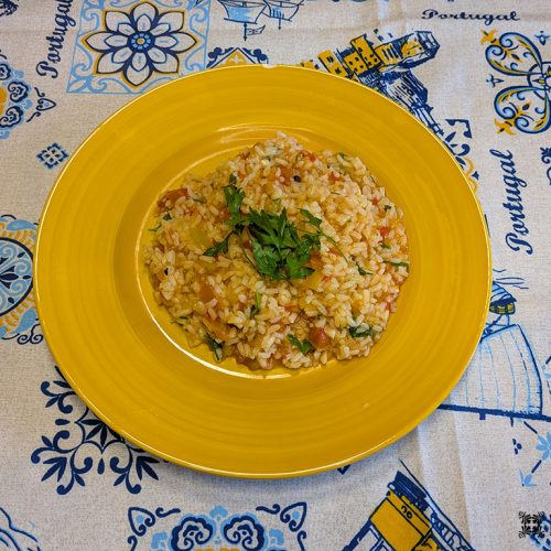 Um prato de arroz de tomate é guarnecido com salsa picada num prato amarelo. A toalha de mesa abaixo apresenta padrões azuis e amarelos.