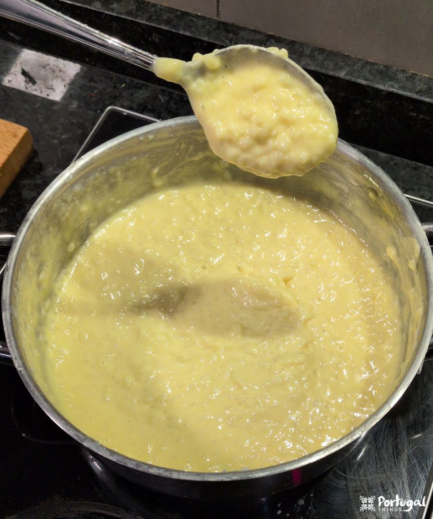 A pot filled with a thick, creamy yellow rice pudding, a traditional recipe, sits on the stovetop. A spoon holds a portion of the rice pudding above the pot, showcasing its rich, comforting texture.