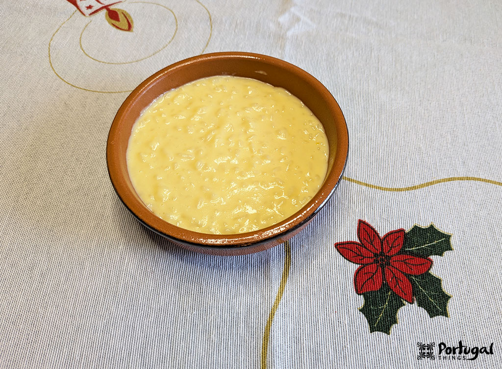 A clay bowl filled with creamy rice pudding sits on a white tablecloth decorated with a red poinsettia and Christmas-themed designs, showcasing a traditional recipe for the beloved rice pudding dessert.