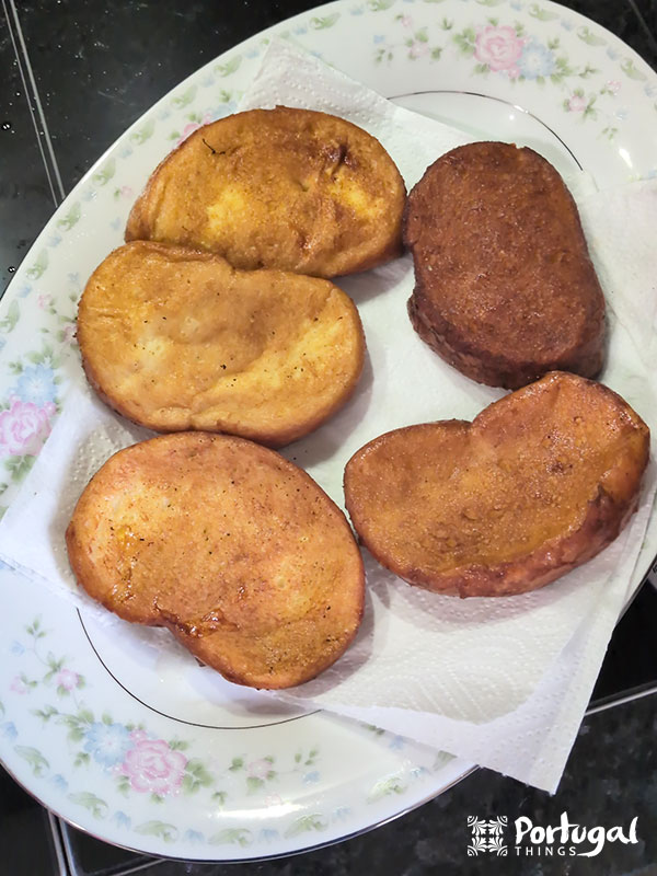 Cinco fatias de Rabanadas de Leite douradas repousam em uma toalha de papel branca em cima de um prato oval com estampa floral. O pão, coberto com uma massa ou mistura de ovos, faz parte de uma receita tradicional. 