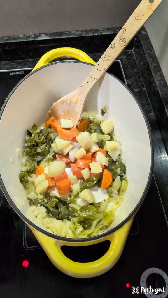 A yellow pot on the stove contains chopped carrots, potatoes, onions, and leafy greens cooking for a traditional Christmas recipe. A wooden spoon rests inside the pot.