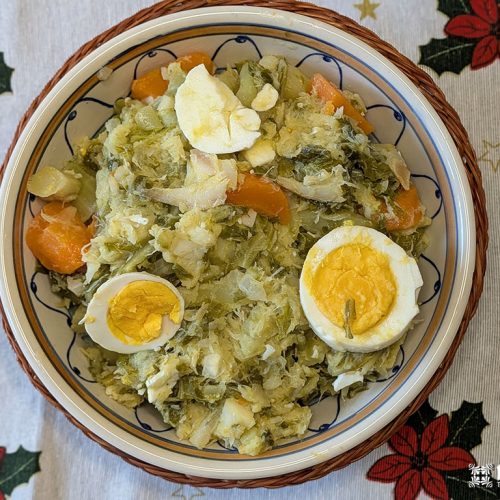Uma tigela do tradicional Roupa Velha português, com bacalhau salgado desfiado, batatas, cenouras, repolho e ovo cozido fatiado, fica sobre uma toalha de mesa festiva - perfeita como uma Receita de Natal para sua reunião de fim de ano.
