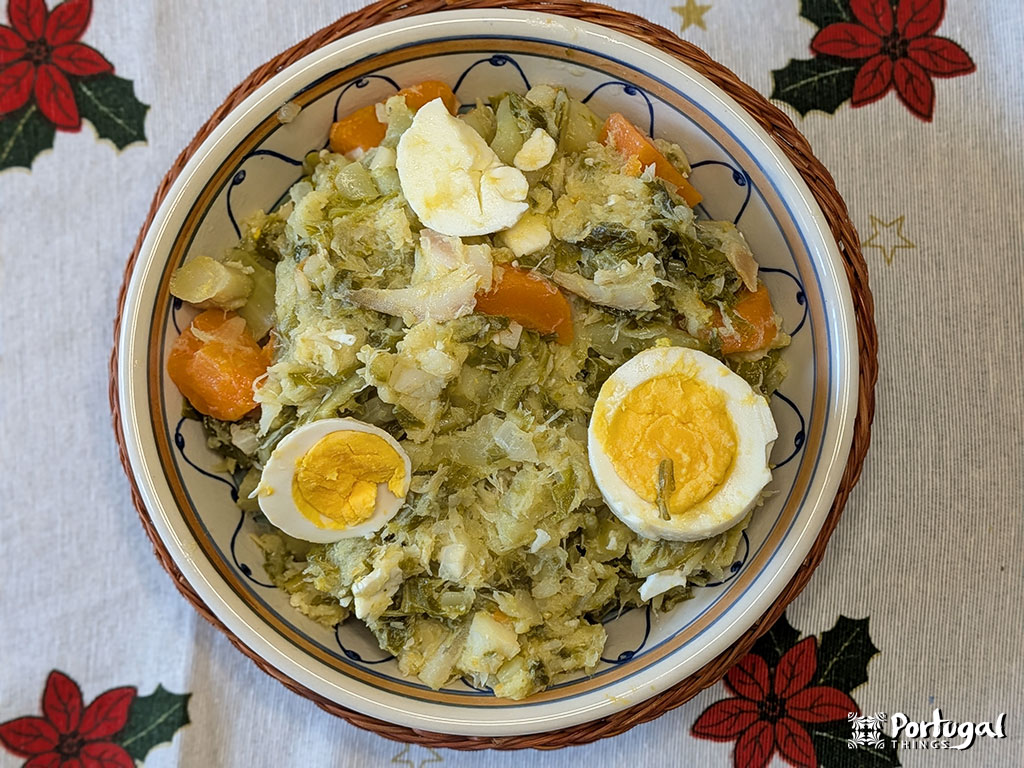 A bowl of traditional Portuguese Roupa Velha, with shredded salted cod, potatoes, carrots, cabbage, and sliced hard-boiled eggs, sits on a festive tablecloth—perfect as a Christmas recipe for your holiday gathering.