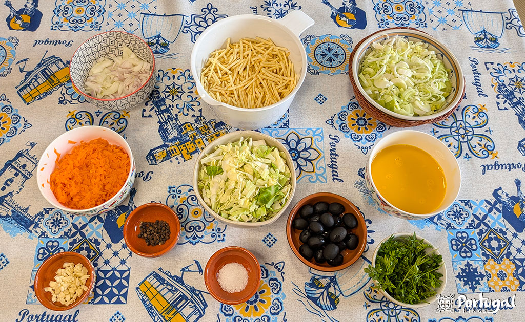 A table laden with chopped vegetables, olives, herbs, and spices surrounds a bowl of yellow liquid, all beautifully arranged on a colorful tablecloth with a Portuguese theme – perfect inspiration for an easy recipe like Legumes à Brás.