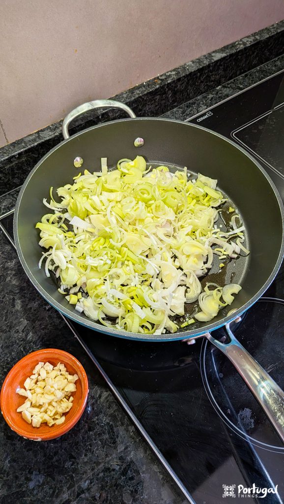 A frying pan sits on the stove with sliced ​​leeks cooking inside, inspired by the traditional Portuguese dish 