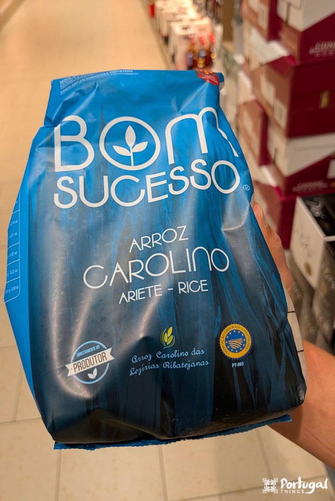 Uma pessoa segura um saco azul de arroz “Bom Sucesso Arroz Carolino”.