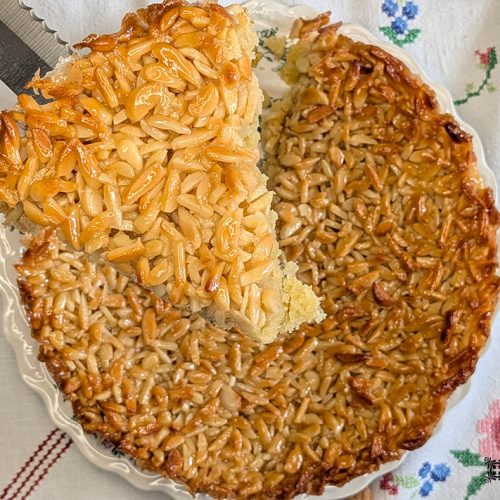uma faca segura uma fatia de tarte de amêndoa, por baixo está uma tarte de amêndoa pronta