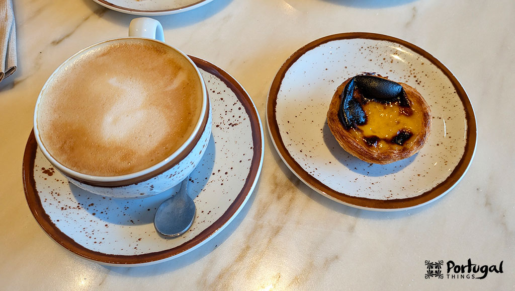 Pastel de nata and a café au lait served on a white saucer