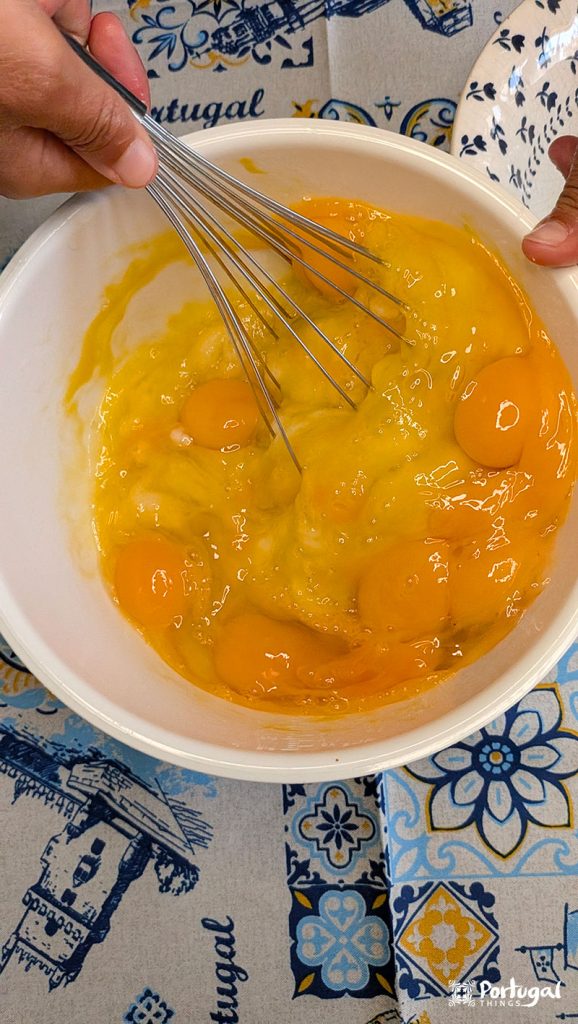 A hand mixes eggs with a wire whisk.