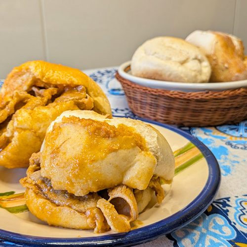 um prato com duas bifanas bem húmidas outro prato mais a trás com dois pães