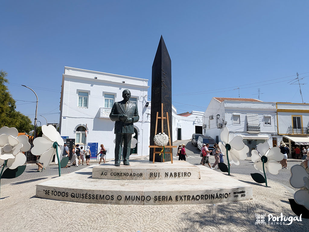 Estatua de rui nabeiro numa praça rodeada de casas brancas em Campo Maior
