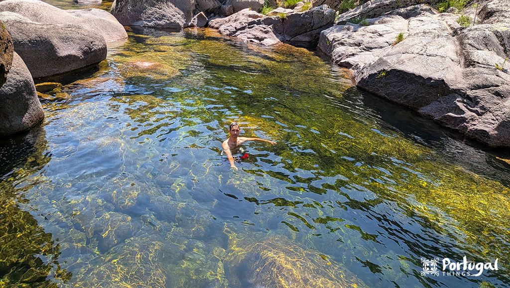 lagoa com agua verde azulada com uma pessoa a nada e rodeada por pedras