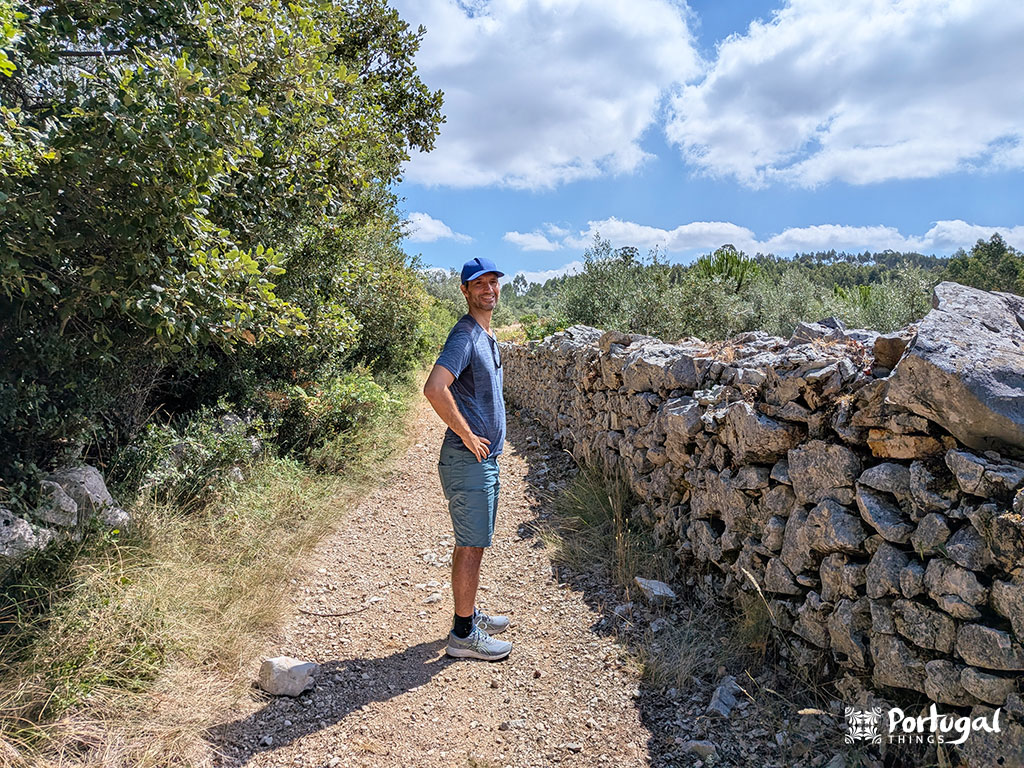 Buracas do Casmilo: Como Fazer o Trilho e Visitar as Grutas 11 uma pessoa ao lado de um muro feito de pedra num trilho