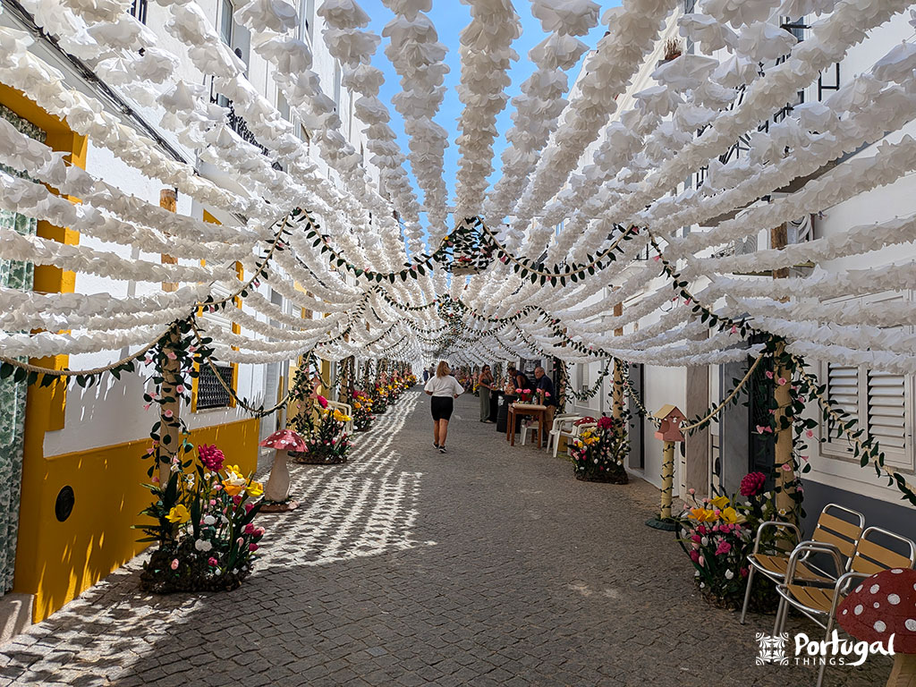 rua com uns enfeites de flores de papel brancas cercada de umas paredes brancas e amarelas