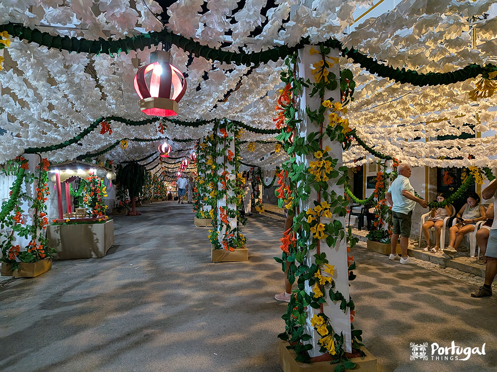 uma rua decorada com flores de papel e moradores sentados em bancos