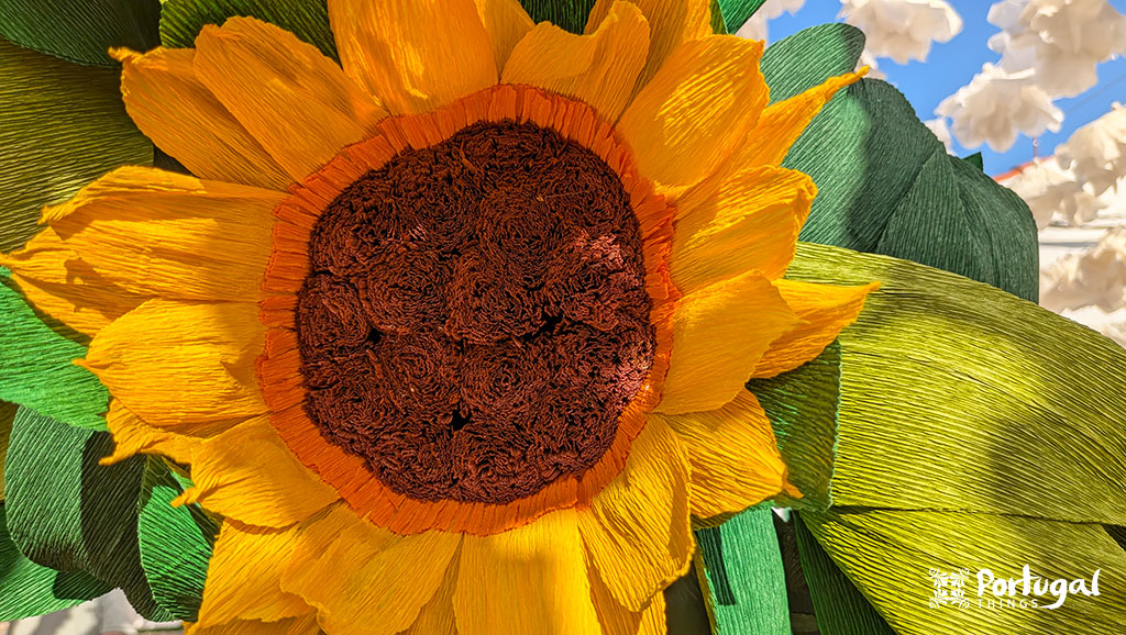 uma flor gira sol feito de papel com pétalas amarelas e folhas verde o interior da flor tem uns pormenores de papel