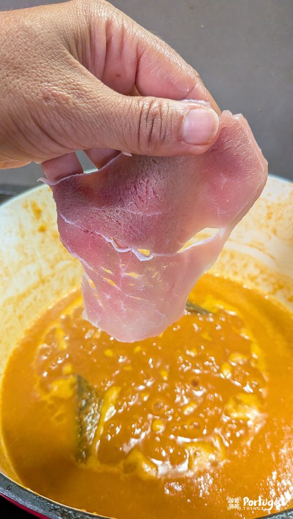 uma mão coloca uma bifana num tacho com molho