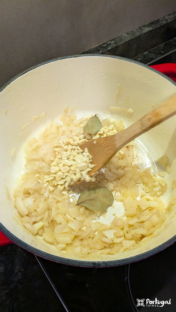 Onion, garlic, and bay leaves being sautéed in olive oil in a saucepan.