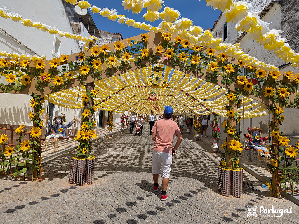 rua enfeitada com umas flores amarelas com uma uma pessoa na entrada da rua com dois espantalhos