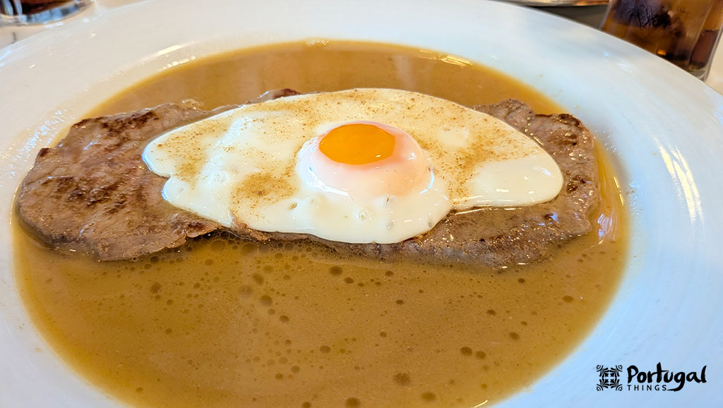 um bife com um ovo à cavalo em cima com um molho cor de avela a rodear o bife