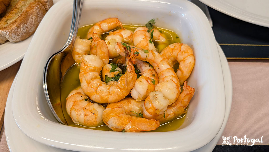 um prato branco com vários camarões médios cobertos com um molho de azeite e varia salsa
