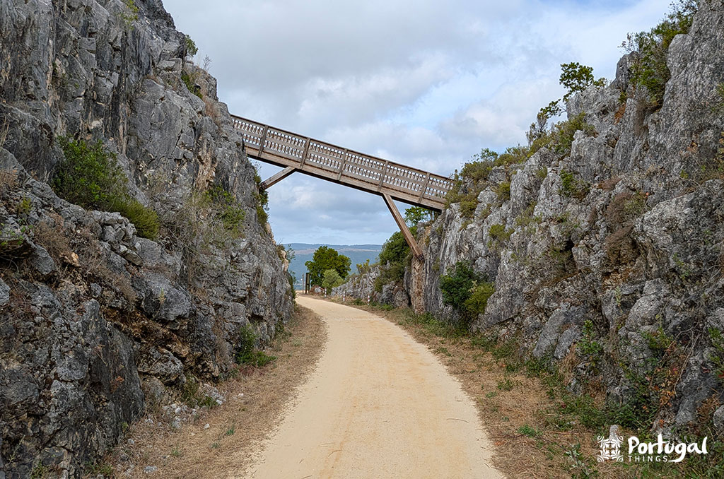 Porto de Mós Ecotrail: Trail, Tunnels, and Windmills 4 Compacted dirt trail marked for bicycles and pedestrians, with a wooden bridge and rocky gorge