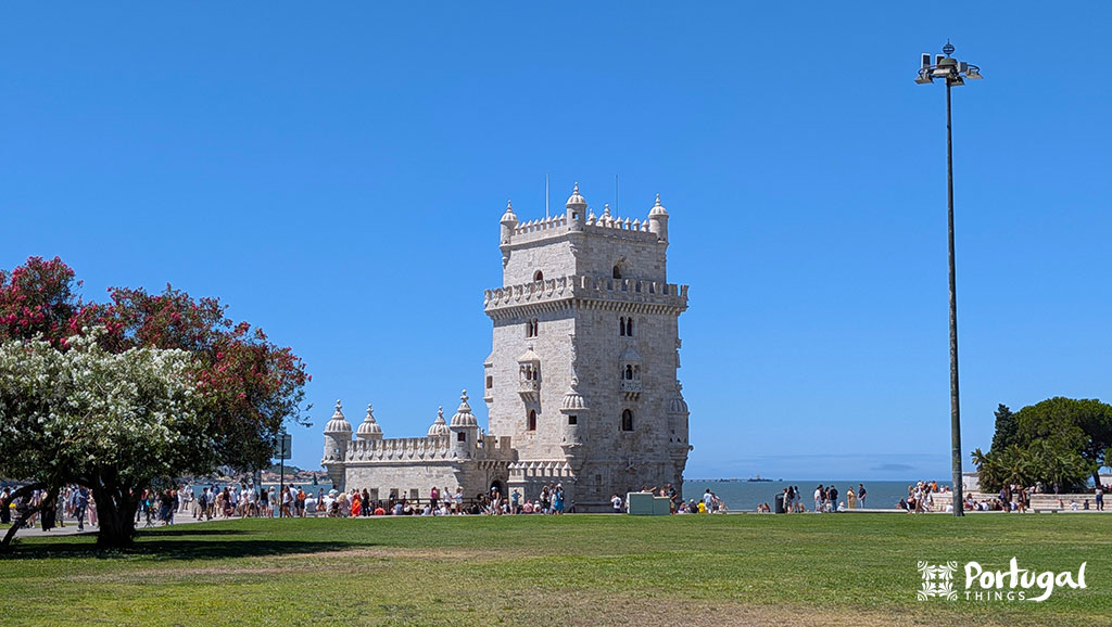 18 best things to do in Lisbon in 3 days - Itinerary 12 A garden with a lawn and trees, with Belém Tower in the background under a bright blue sky.